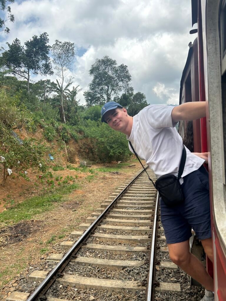 Reiziger leunt uit de open deur van de trein met uitzicht over het bergland van Sri Lanka