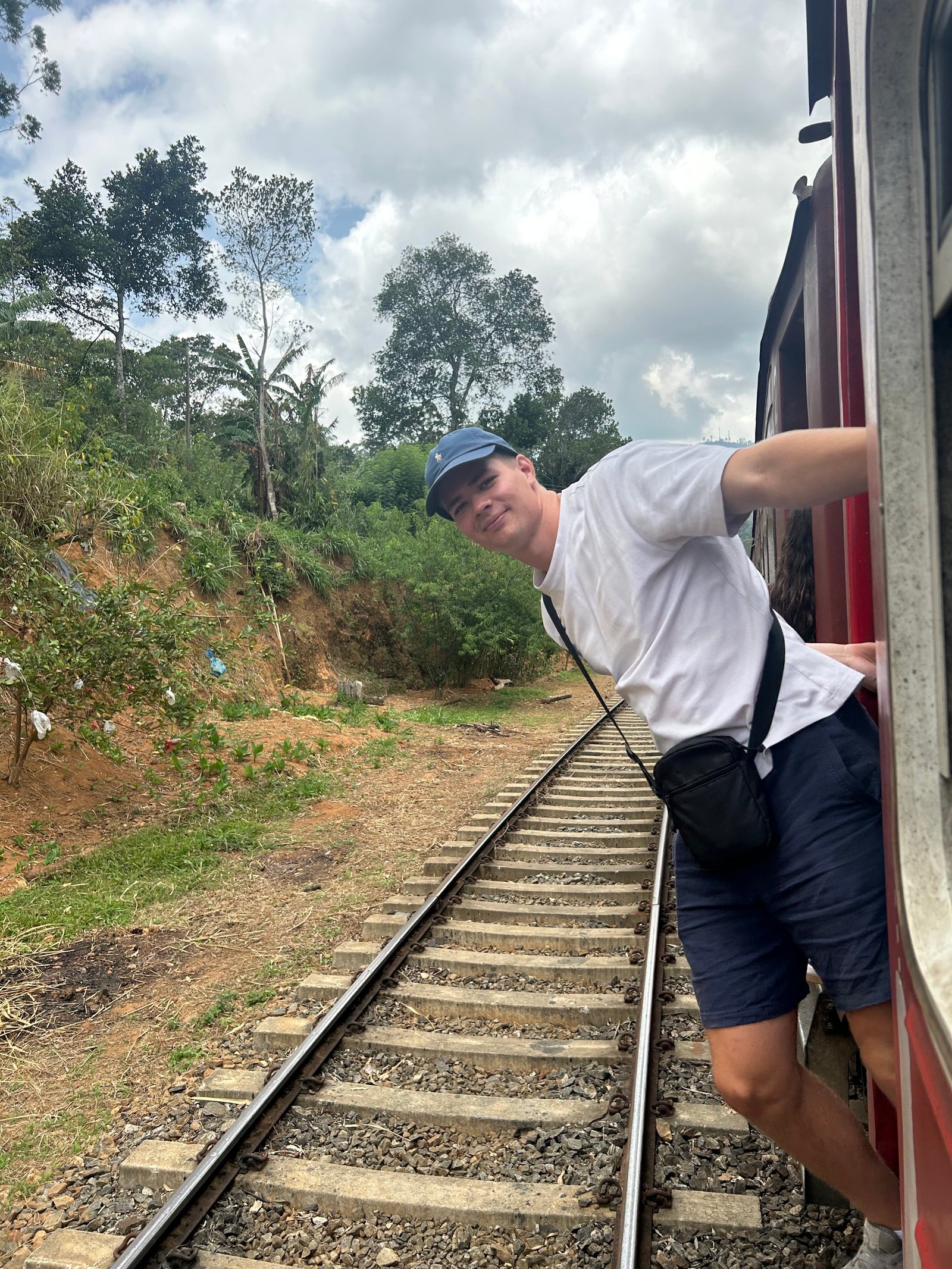 Reiziger leunt uit de open deur van de trein met uitzicht over het bergland van Sri Lanka