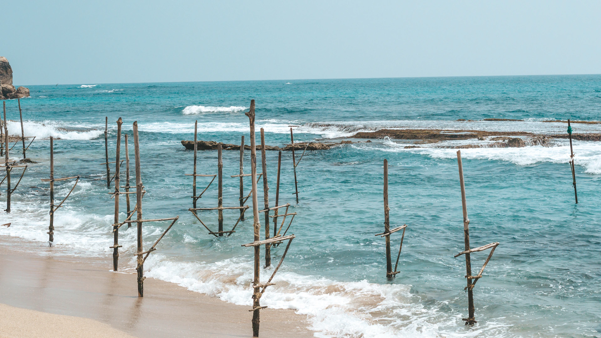 Houten palen van de stikvissers steken uit boven het water bij Weligama