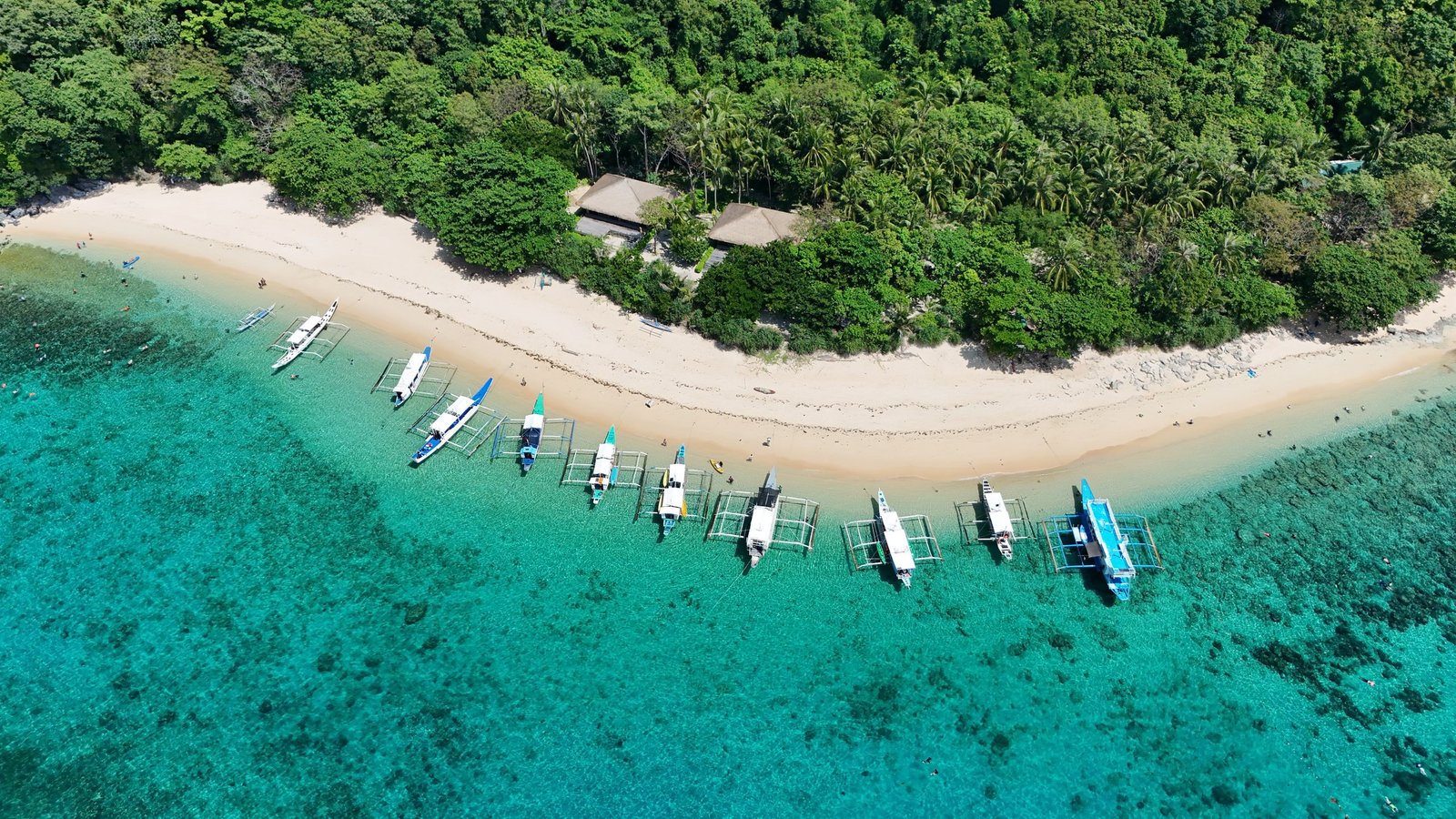 Luchtfoto van bangkaboten die aangemeerd liggen op een turquoise strand bij El Nido in de Filipijnen