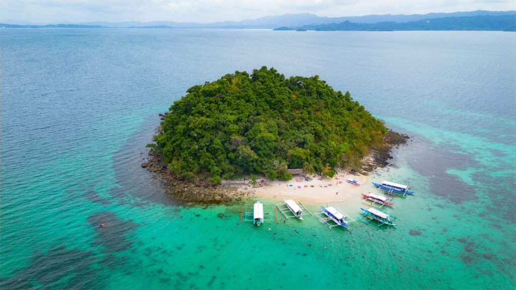 Klein eiland met wit strand en bangka’s voor de kust van San Vicente op Palawan