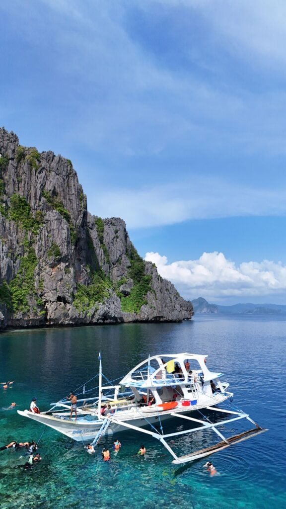 Bangka met snorkelaars bij een rotswand tijdens een eilandhoptour bij El Nido