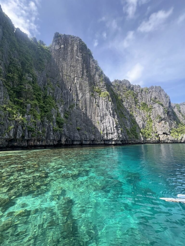 Steile kalkrots boven helder turquoise water tijdens een eilandhoptour bij El Nido