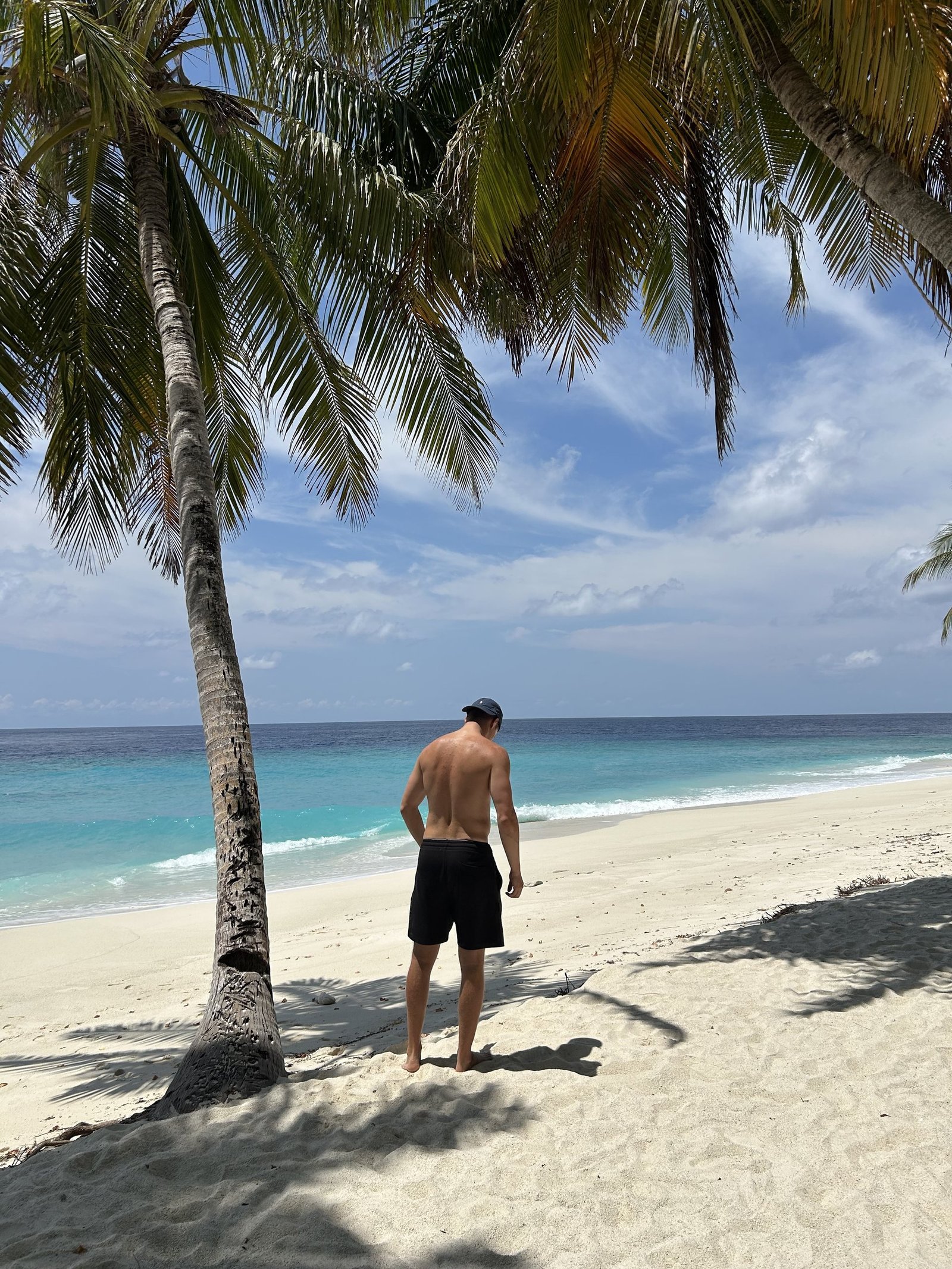 Mitchel loopt onder de palmbomen over het strand van een lokaal eiland op de Malediven