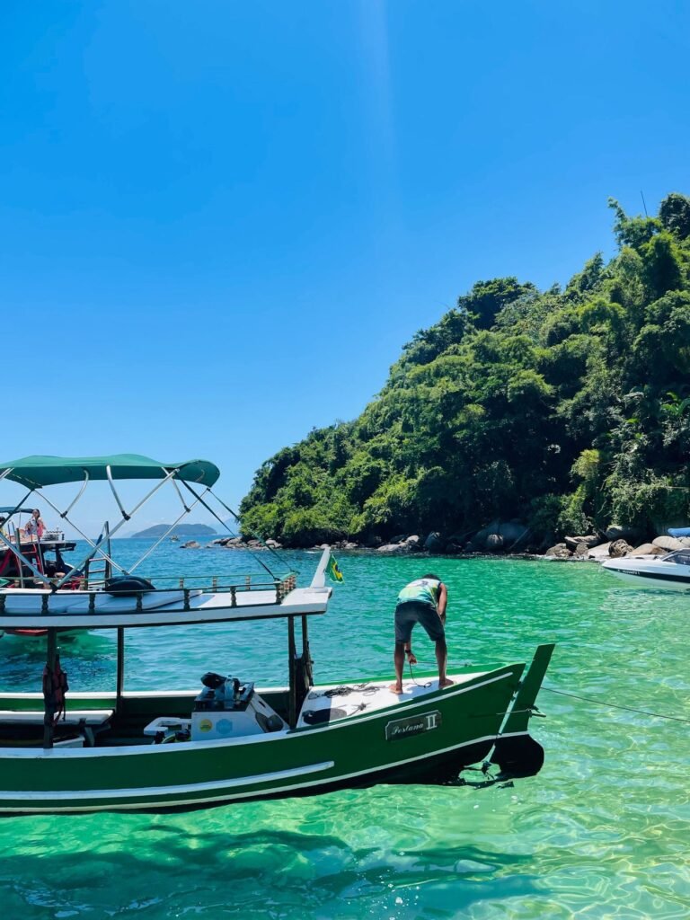 Boot in helder turquoise water langs een beboste kust bij Paraty