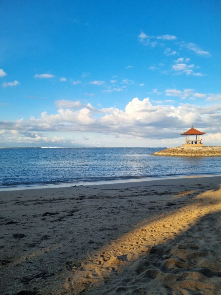 Strand van Sanur met palmen en een balé in de verte