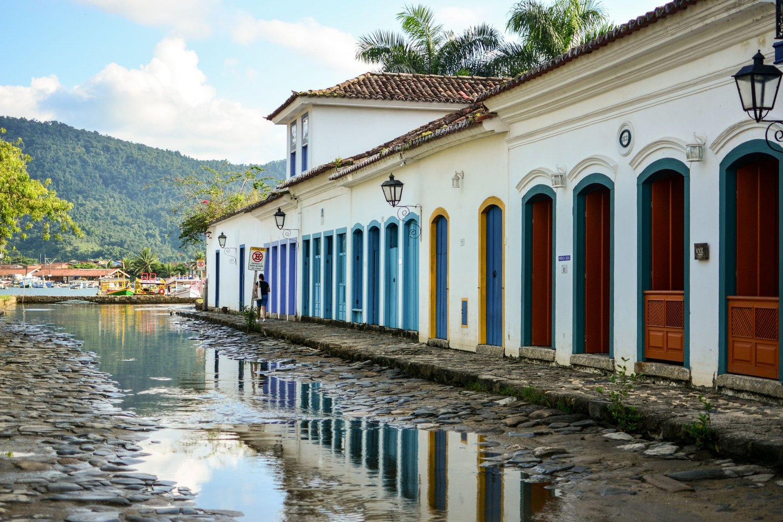 Witte koloniale huizen in Paraty weerspiegeld in het water, met de bergen op de achtergrond