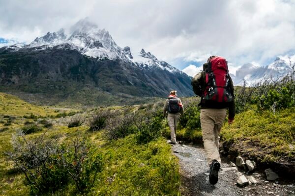 Twee wandelaars met rugzak lopen over een bergpad richting besneeuwde toppen