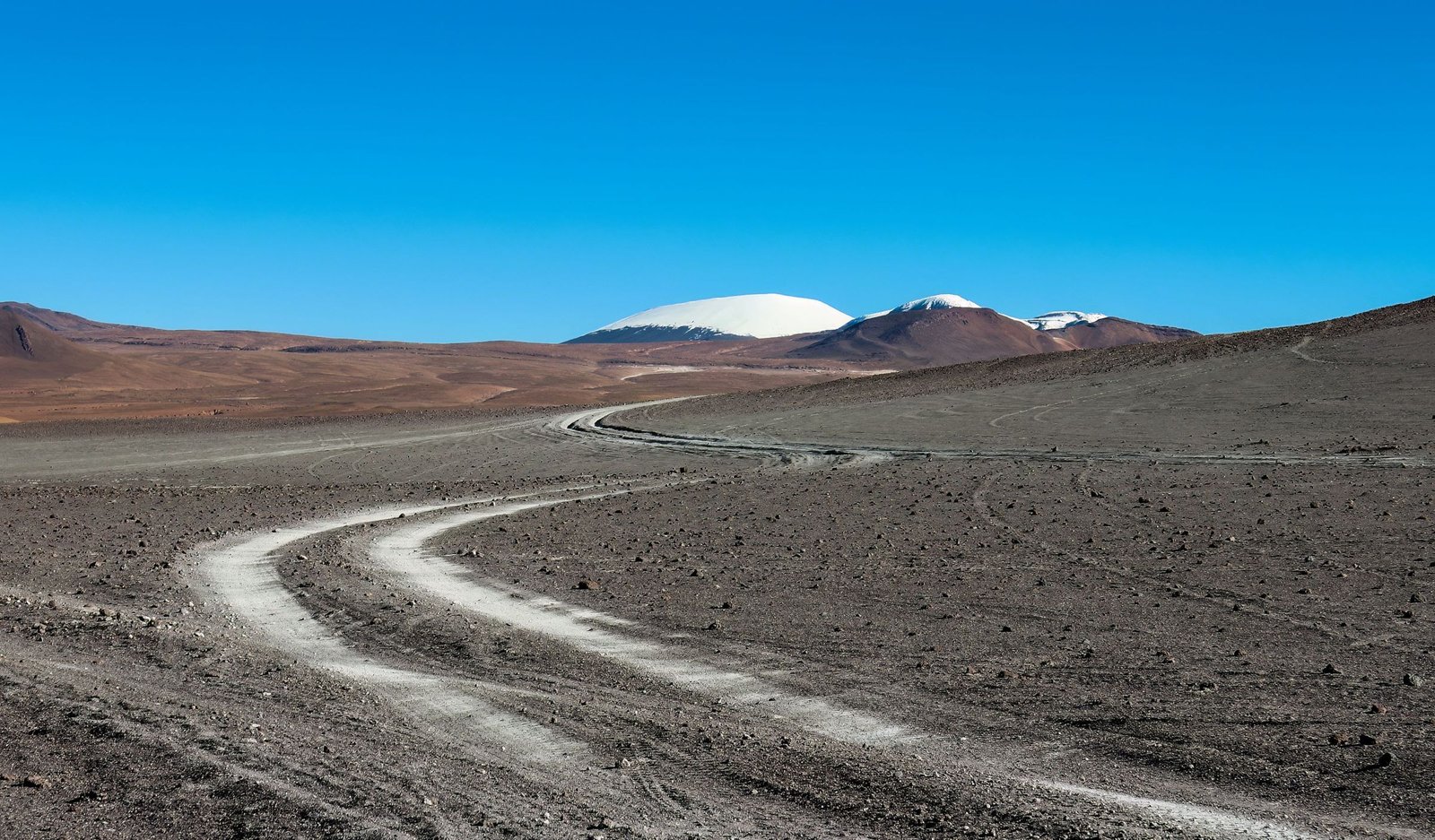 Weg door een droog landschap richting besneeuwde bergen in Bolivia