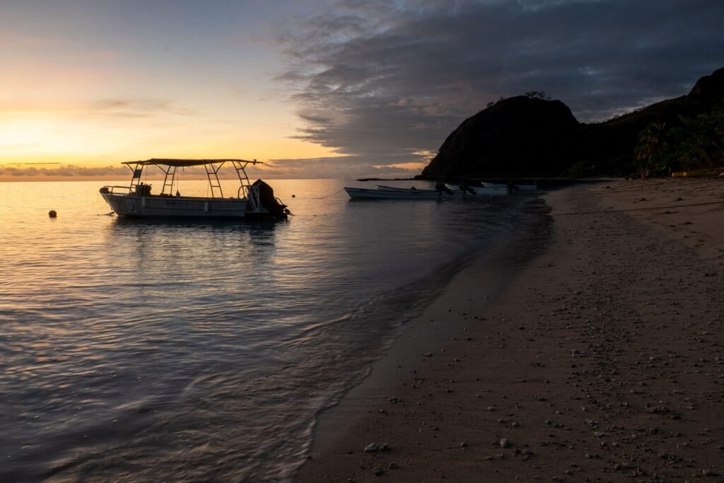 Zonsopkomst boven een rustig strand met een boot in Fiji