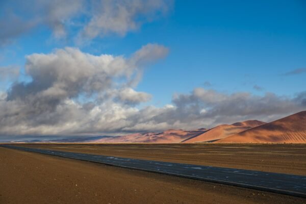 Asfaltweg door de Namib met rode duinen in de verte